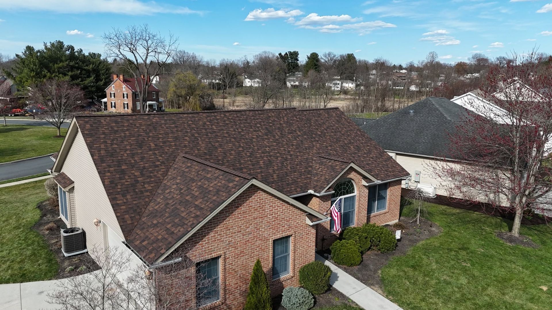 Aerial view of a brick house with a brown roof and a person standing on the front walkway