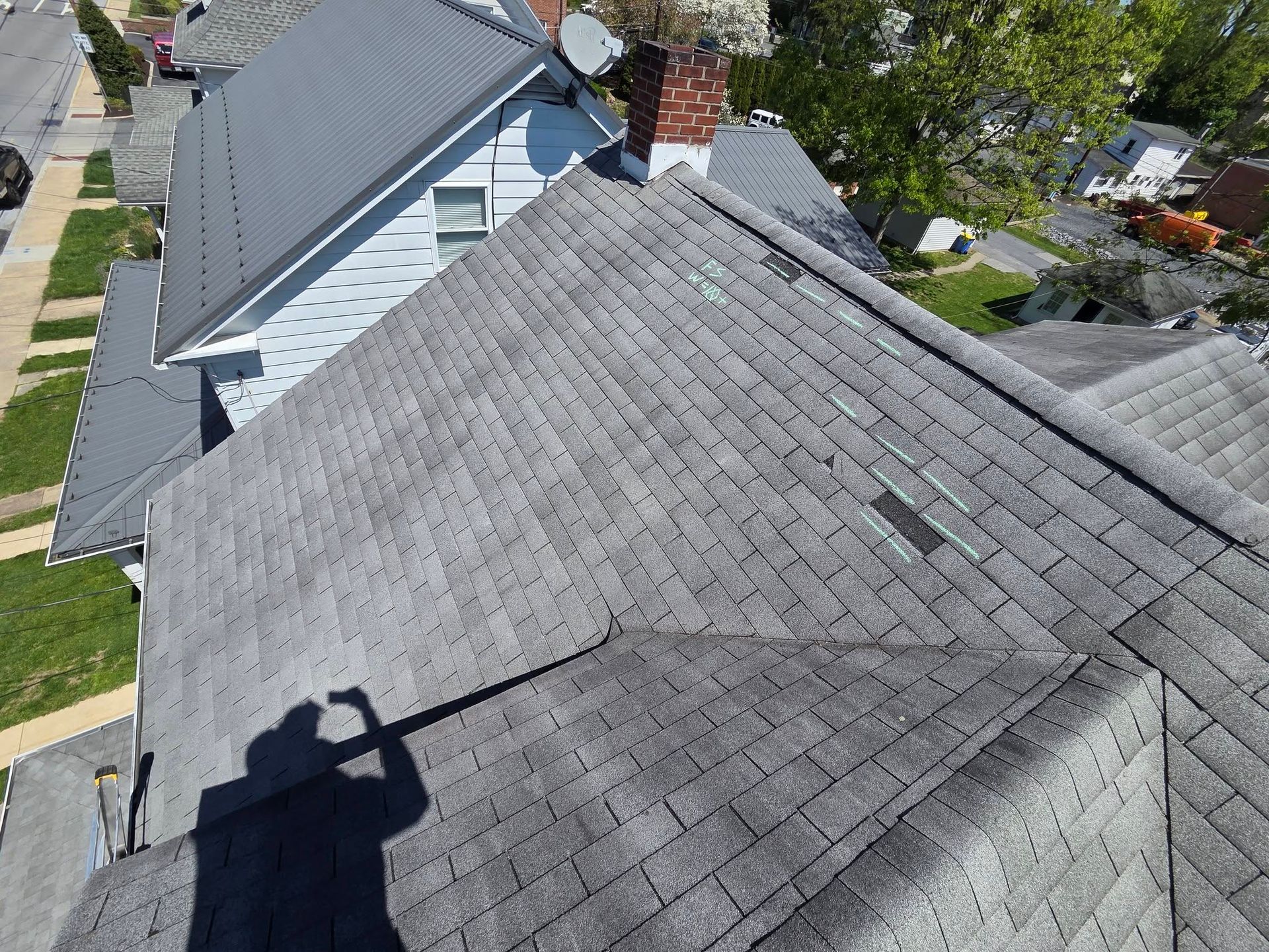Aerial view of gray shingled house roofs with a rooftop shadow and neighboring homes below.