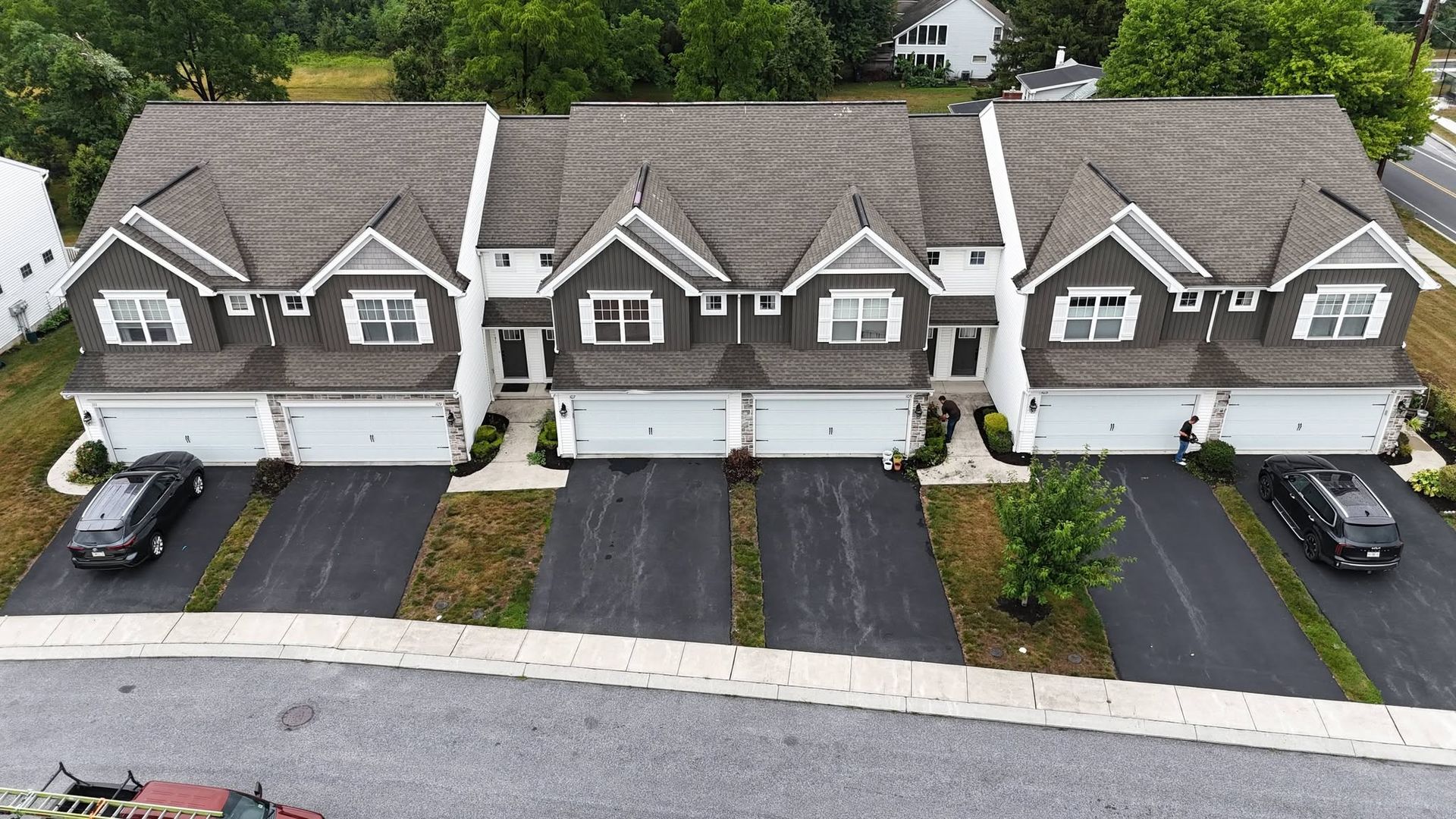 Row of three gray townhouses with white trim and black driveways on a suburban street