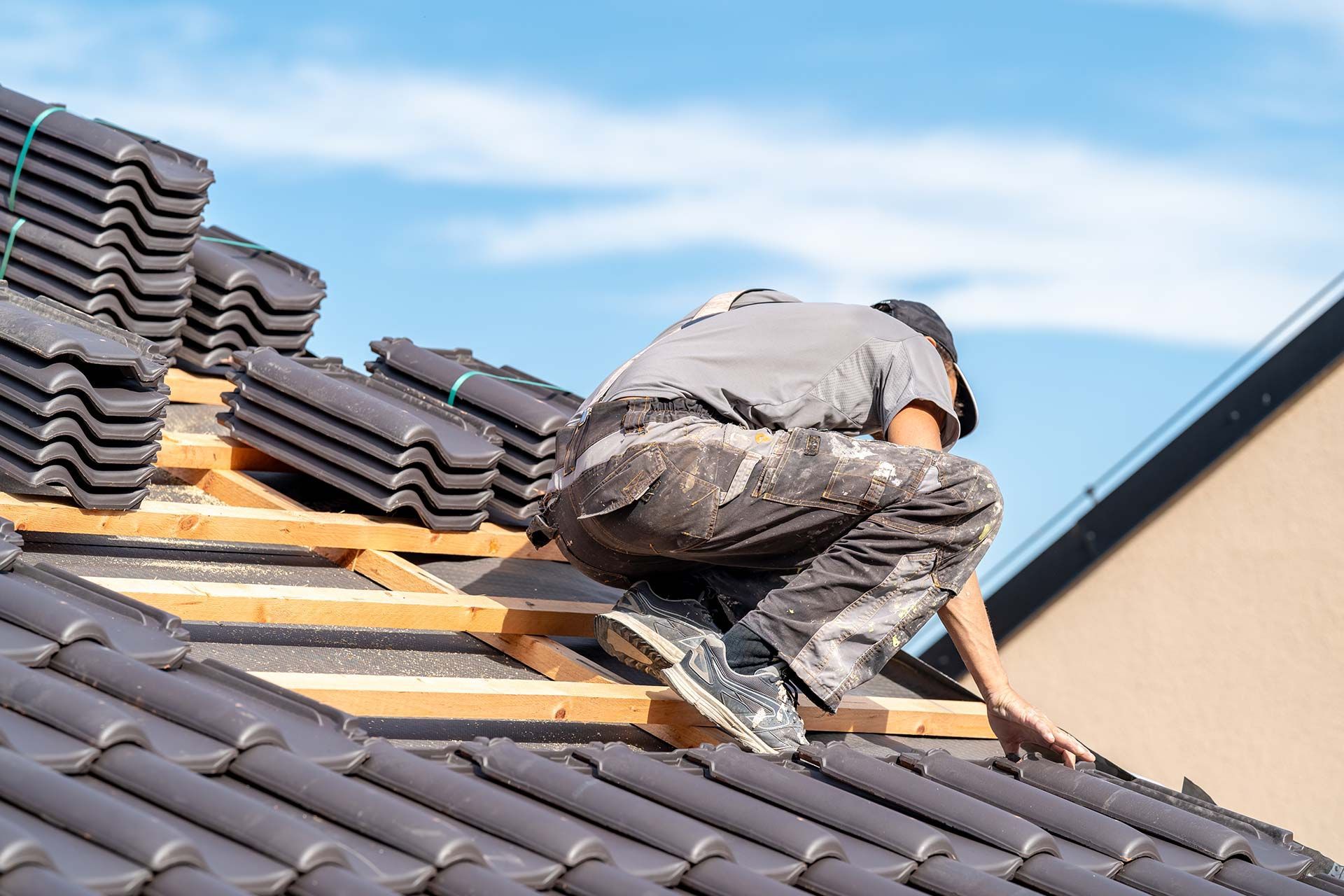 Worker installing roof tiles on a house roof under a blue sky