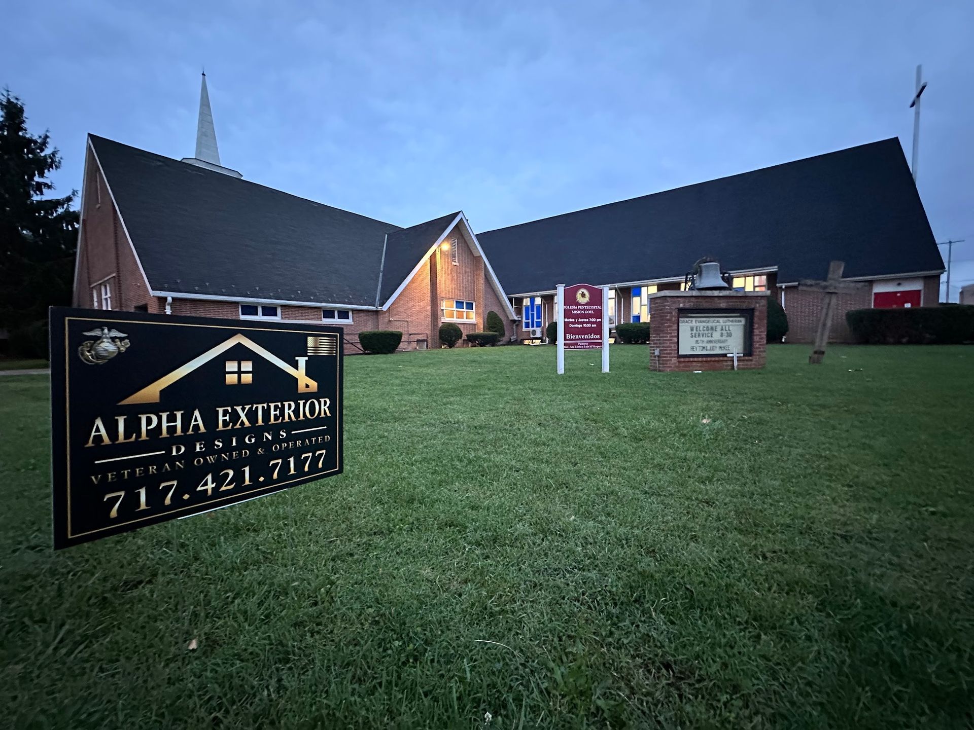 Exterior of a brick church at dusk with an Alpha Exterior Services sign on the lawn