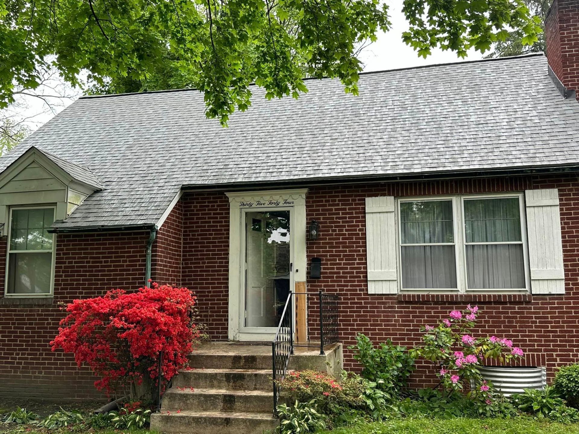 Brick house with gray roof, white-trimmed windows, front steps, and colorful shrubs in the yard