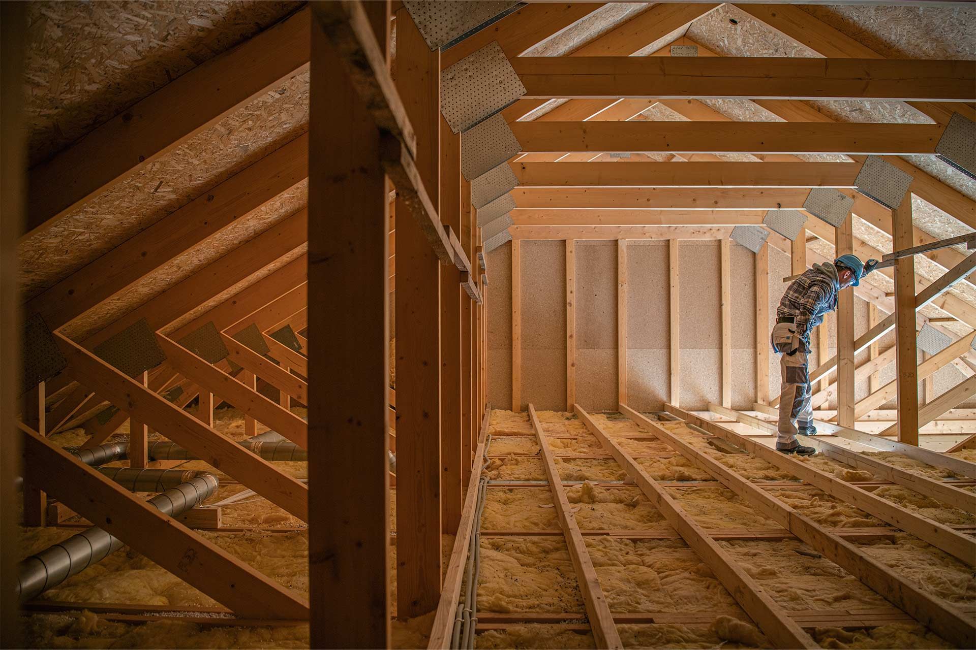 Wooden attic framing with exposed beams and rafters, lit by warm sunlight through the roof opening