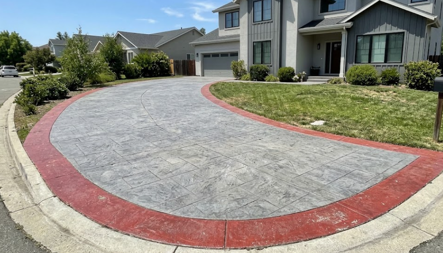 A durable decorative concrete driveway featuring a gray slate pattern and a distinct red brick border leading to a modern house.