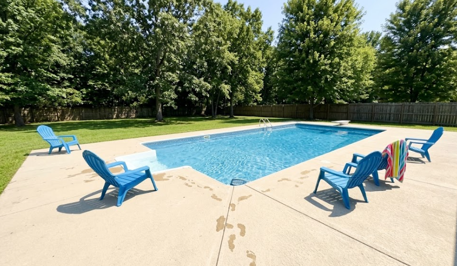 A slip-resistant decorative concrete pool deck in a soft beige color surrounding a bright blue swimming pool with lounge chairs.