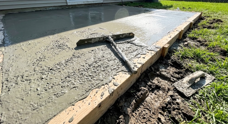 Concrete contractors smoothing a freshly poured backyard patio slab.
