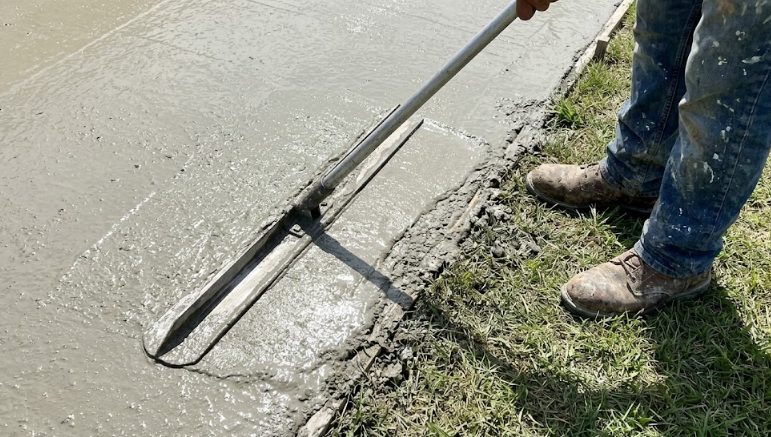 Concrete contractor smoothing wet cement with a bull float tool.
