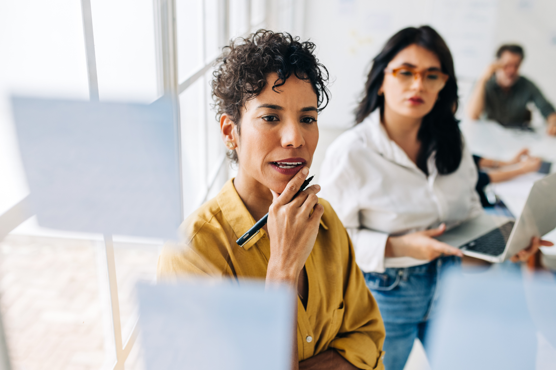 Two women brainstorming and looking at sticky notes on a glass wall.