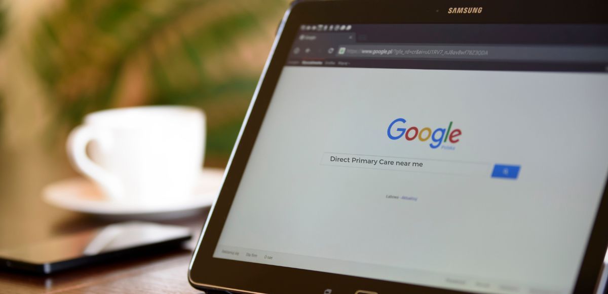 Laptop showing Google homepage beside a blurred coffee cup on a desk