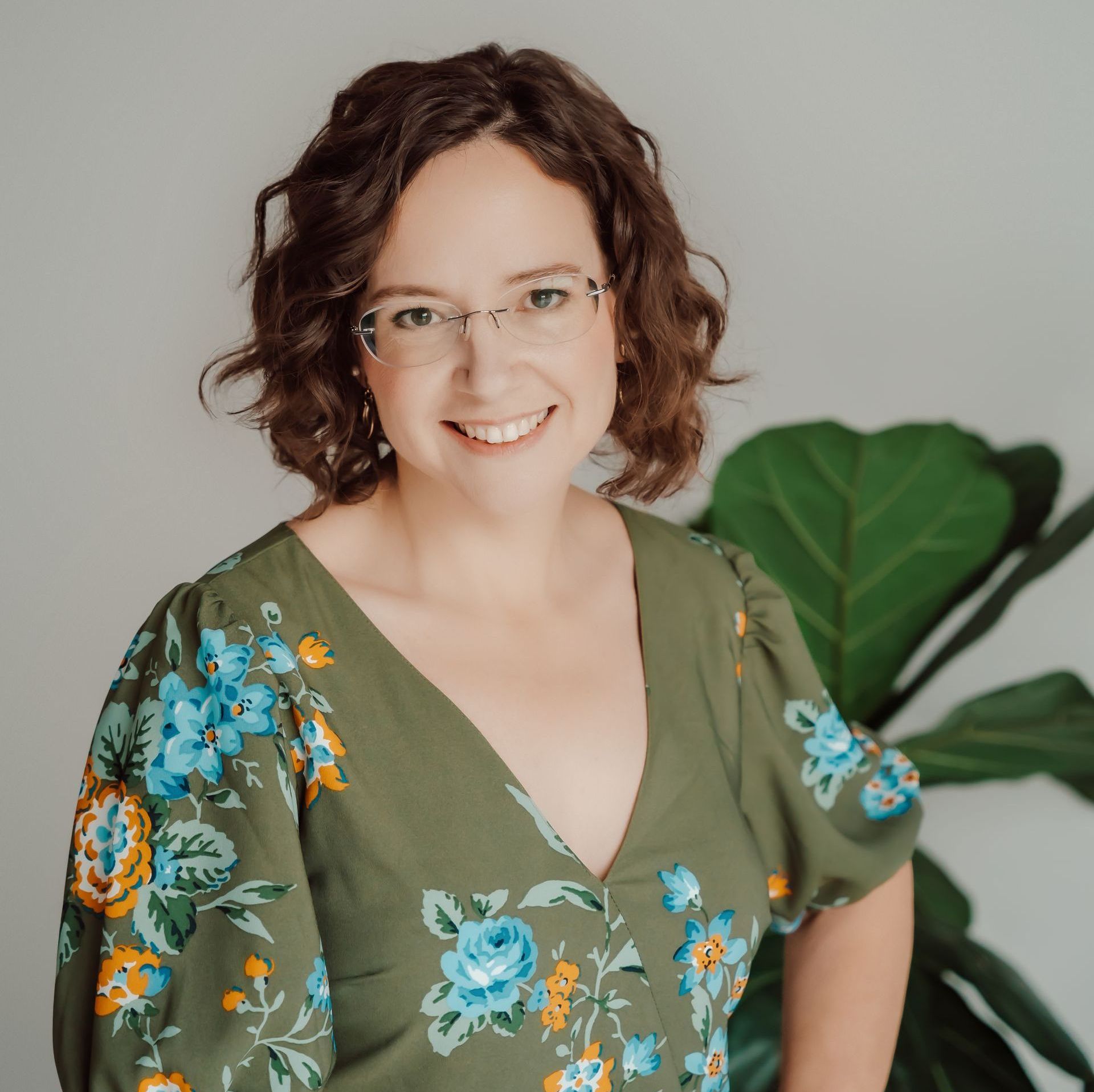 A woman wearing glasses and a green floral dress is smiling for the camera.