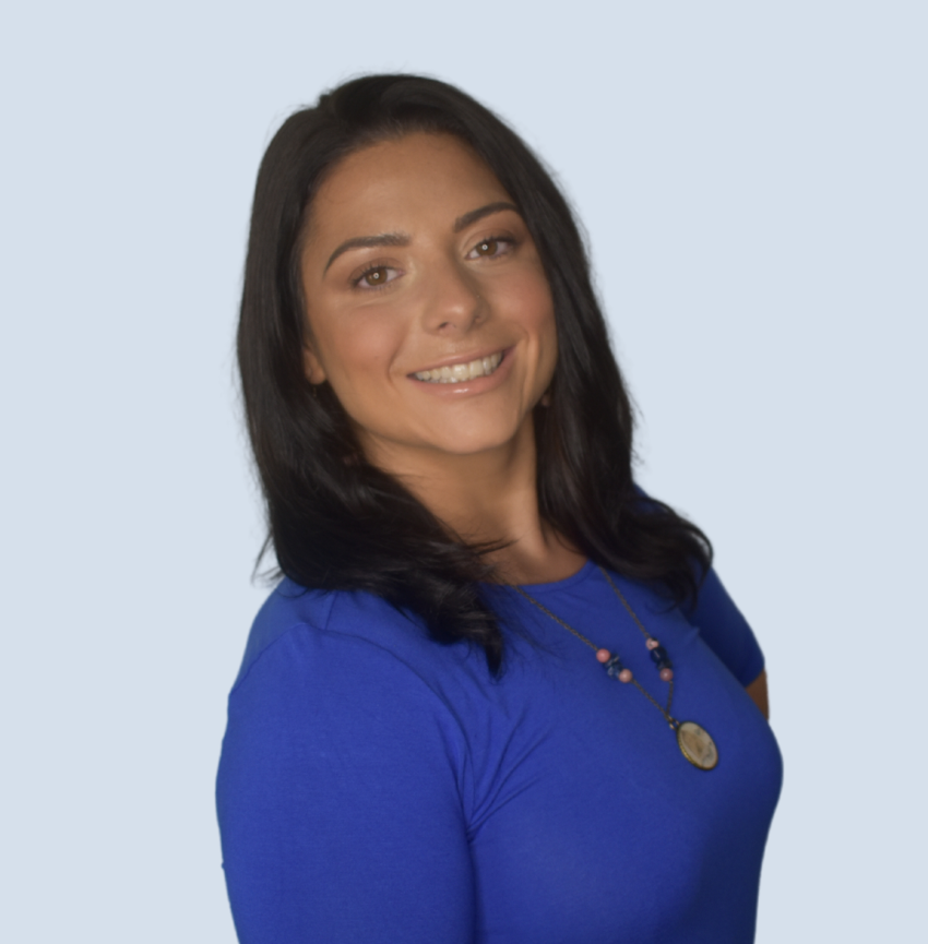 A woman in a blue shirt and necklace smiles for the camera
