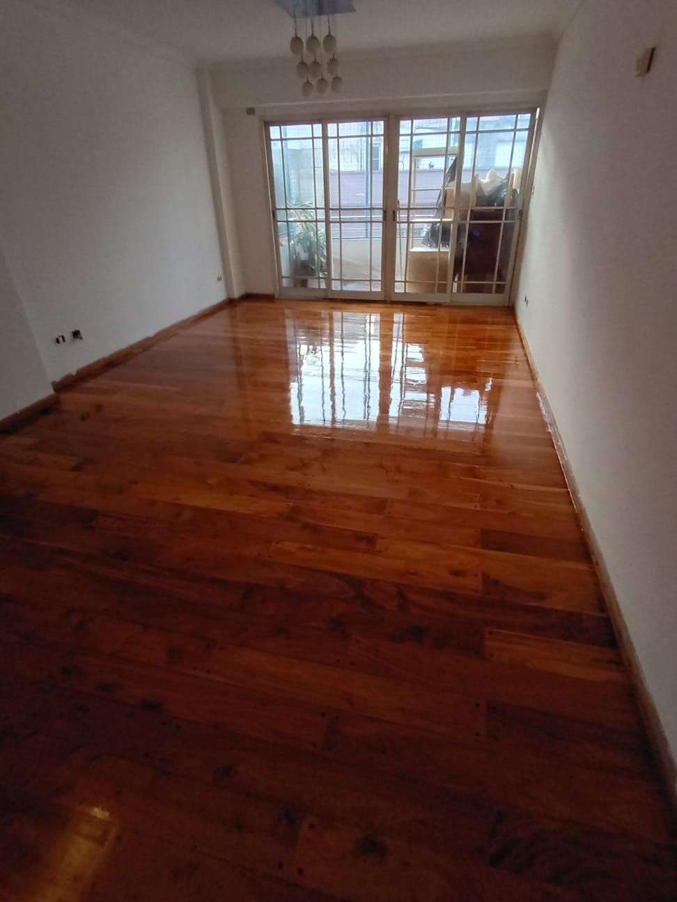 Habitación vacía con suelo de madera pulida y puertas correderas de cristal que dan a un balcón.