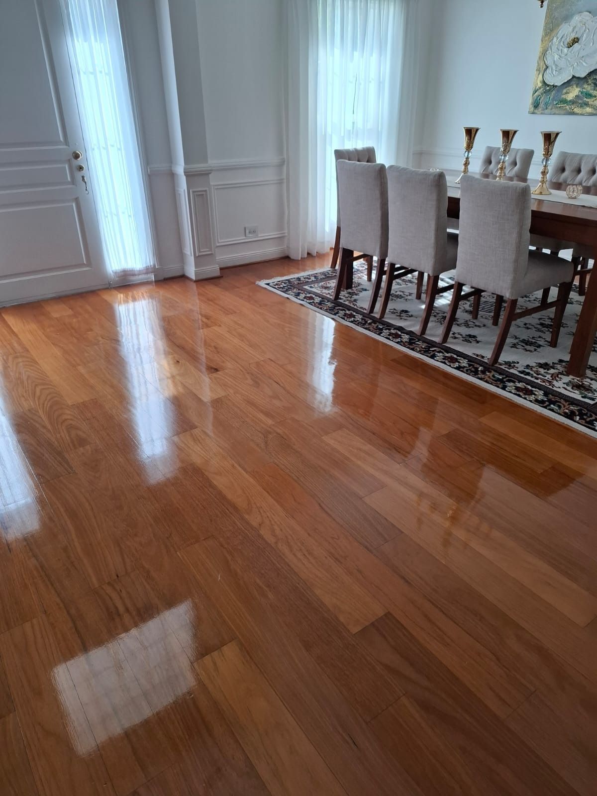 Comedor de madera noble pulida con sillas y mesa blancas junto a grandes ventanales.