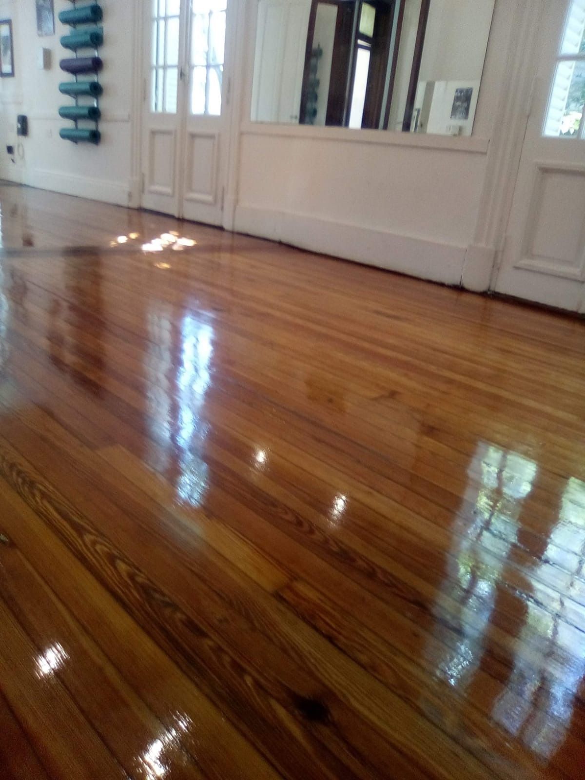 Un reluciente suelo de madera noble en una habitación vacía con paredes y puertas blancas, que refleja la luz de la ventana.