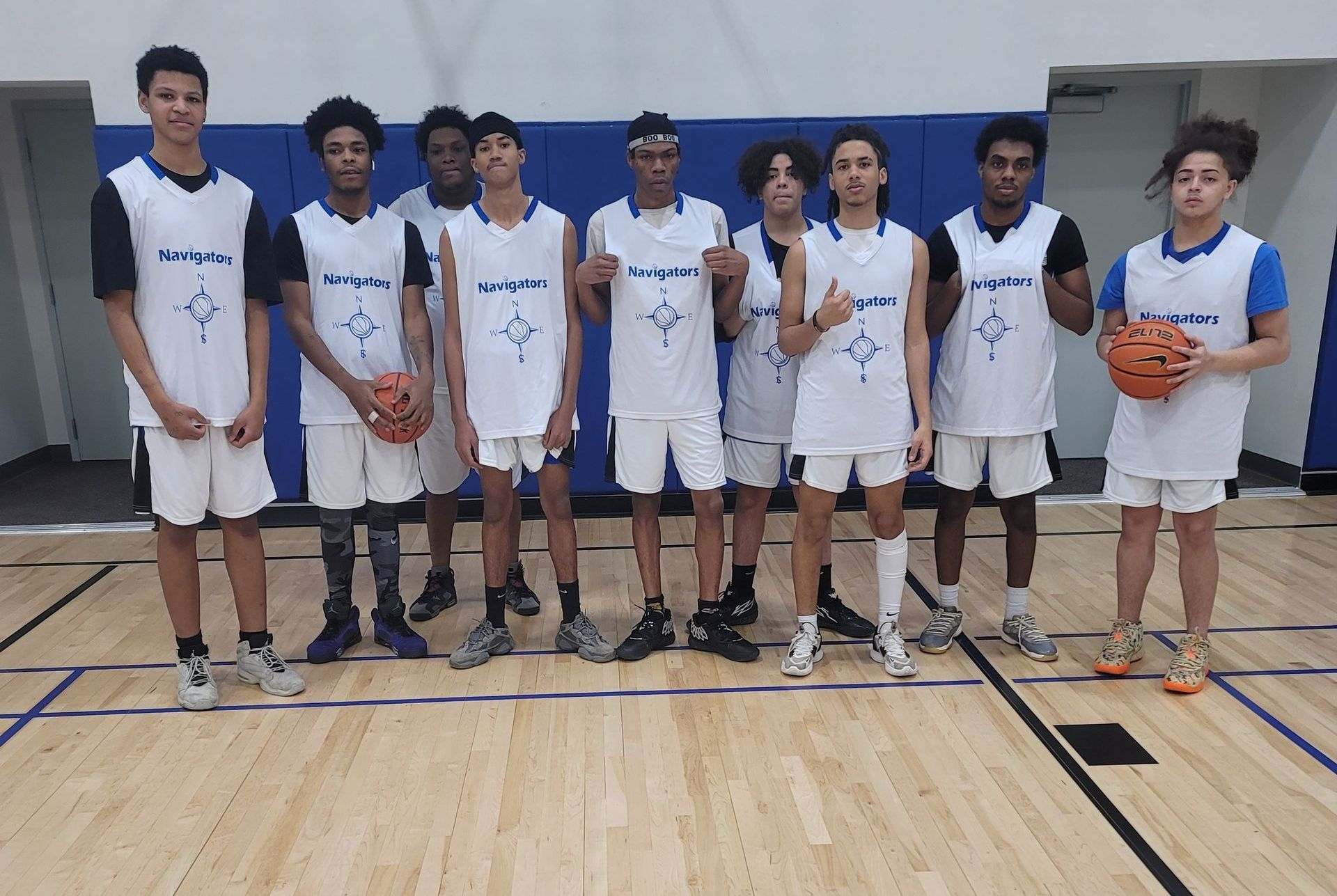 Seven basketball players in white uniforms posing on an indoor court, one holding a basketball.