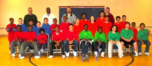 Group seated and standing in a gym, wearing red and green shirts for a team photo.