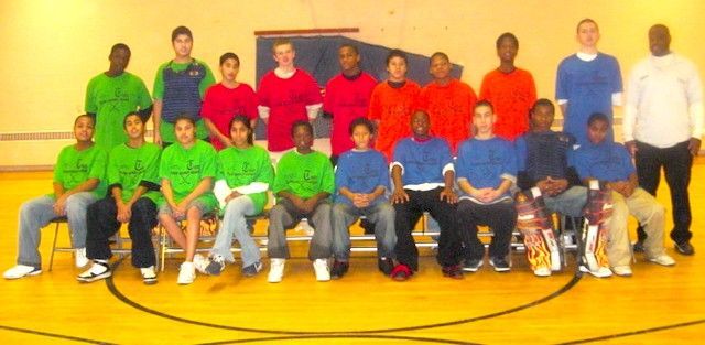 Group of people posing in colorful shirts on a gym floor with basketball court lines visible