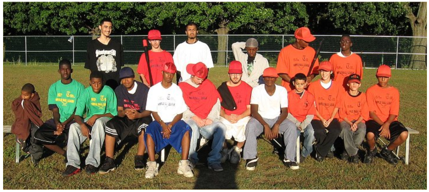 Youth baseball team and coaches posing on a field in bright green, white, red, and orange uniforms