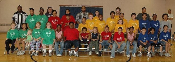 Group of children and adults posing in colorful team shirts in a gymnasium