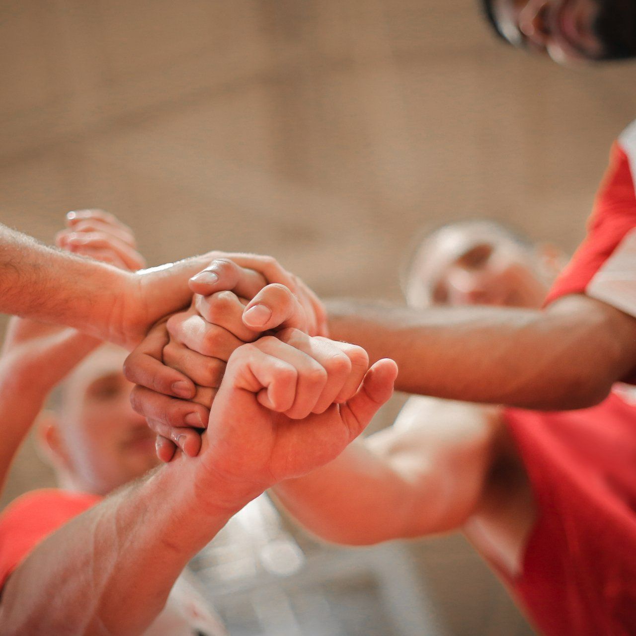 Hands stacked together in a team huddle, with red shirts blurred in the background