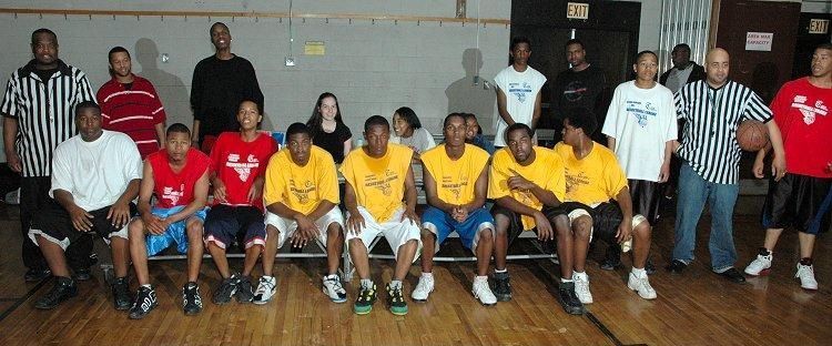 Group photo of basketball players and coaches posing in a gymnasium, with seated players in red and yellow jerseys