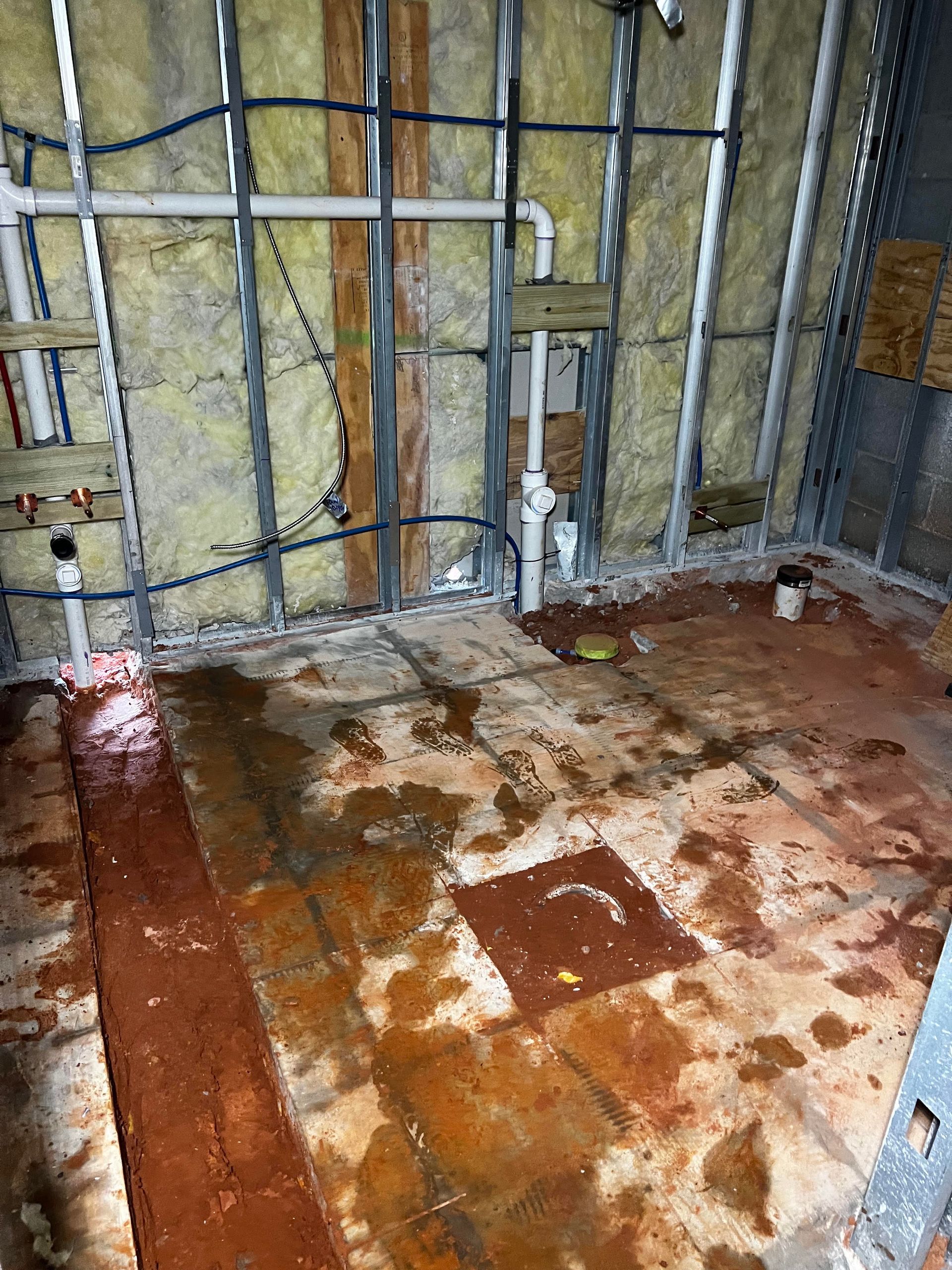 Basement wall framing with exposed insulation and damp, rust-stained concrete floor with debris