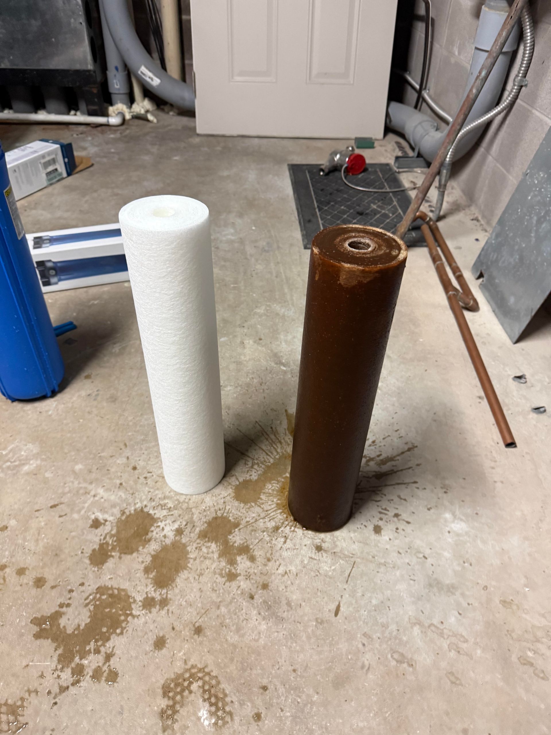 Two vertical pipes, one white and one rusty brown, standing on a concrete floor in a utility area