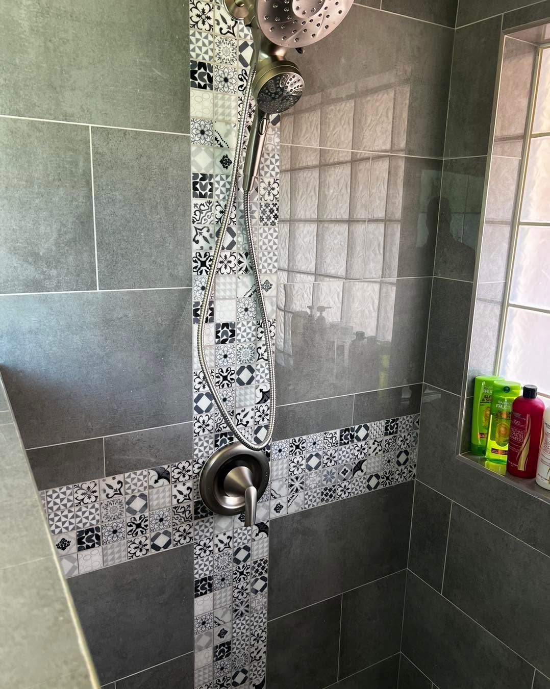 Tiled shower with gray walls, decorative mosaic strip, and a showerhead above a built-in shelf with toiletries