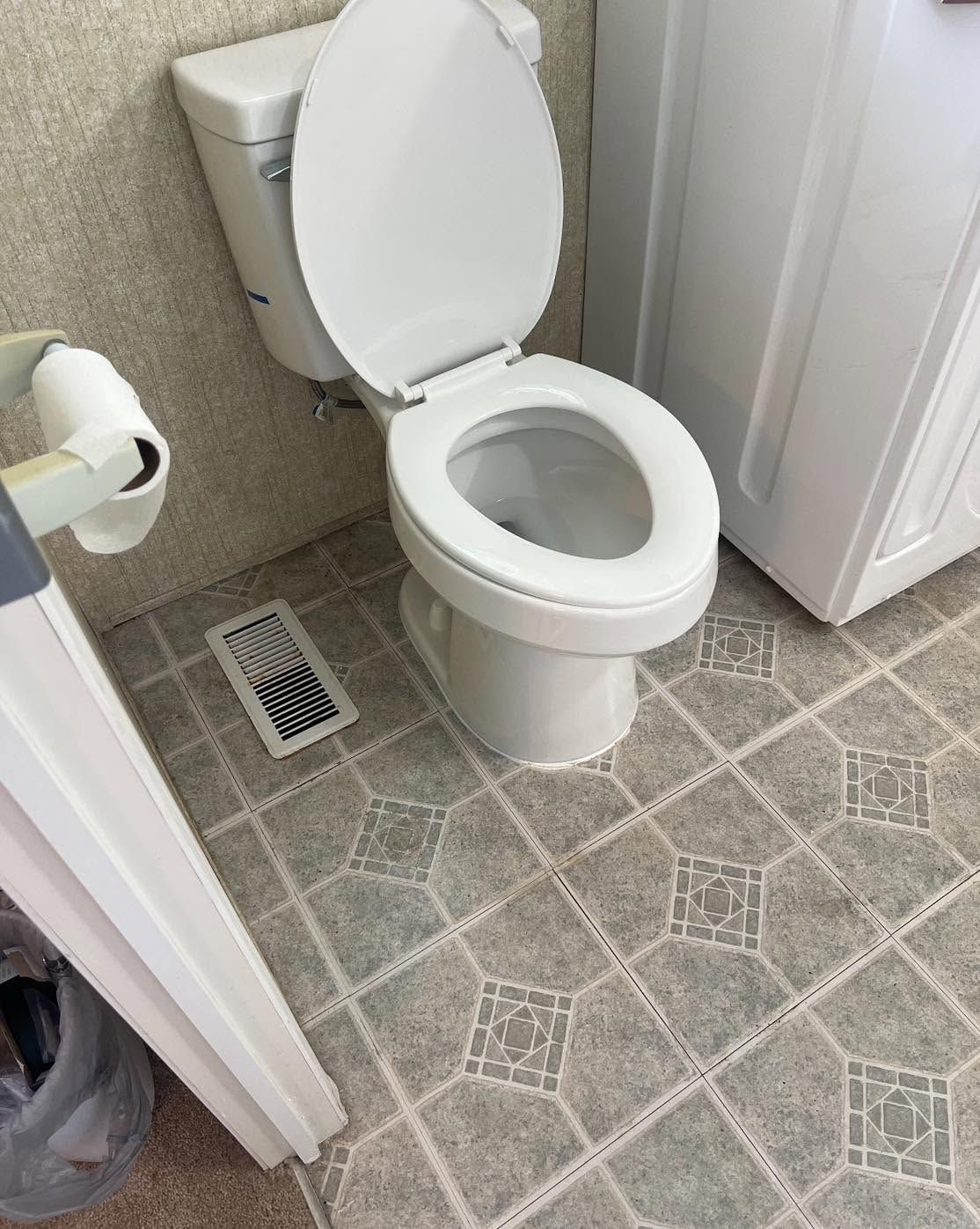 Small bathroom with a white toilet, gray patterned floor, and a wall vent near the door.