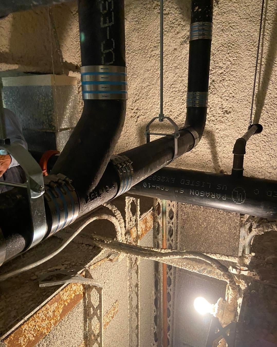 Ceiling pipes and ducts in an unfinished industrial space, lit by a bright work light.