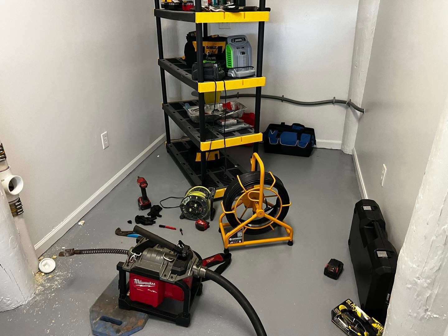 Utility closet with a black/yellow shelf, tools, a red machine, and an orange hose reel on the floor.