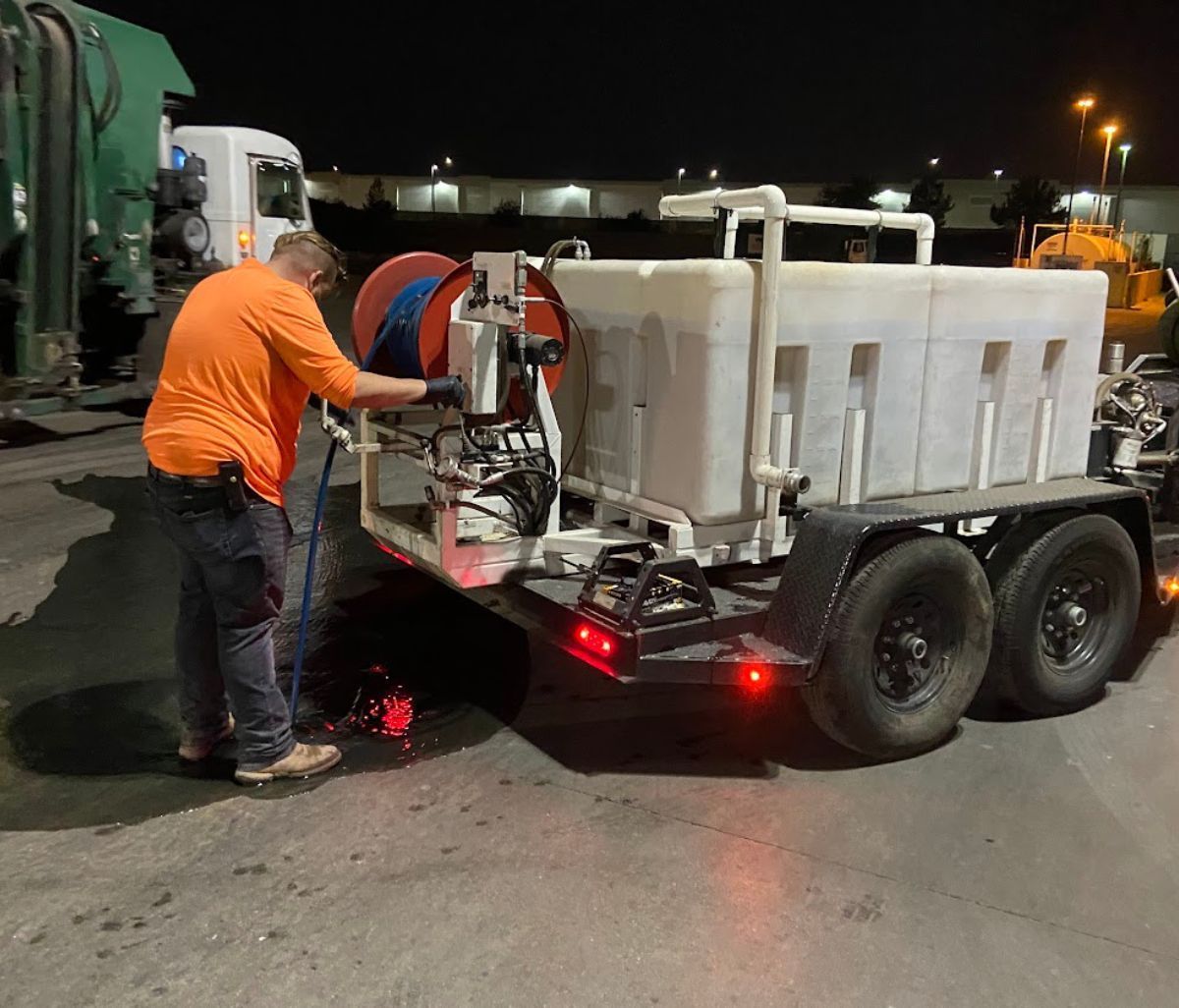 Worker in orange shirt refills a street sweeperβs water tank at night