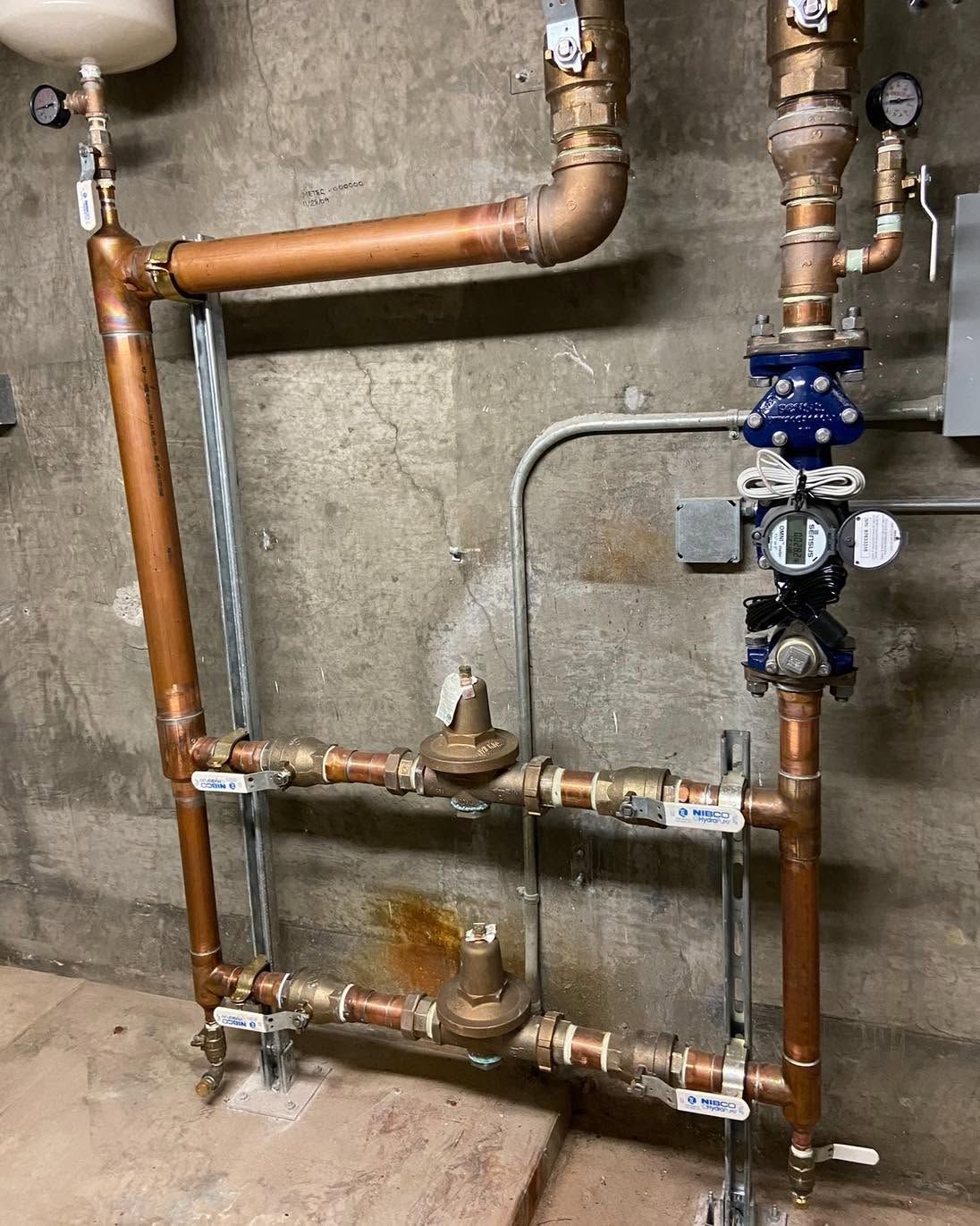 Copper and galvanized pipes with valves on a concrete wall in a utility room