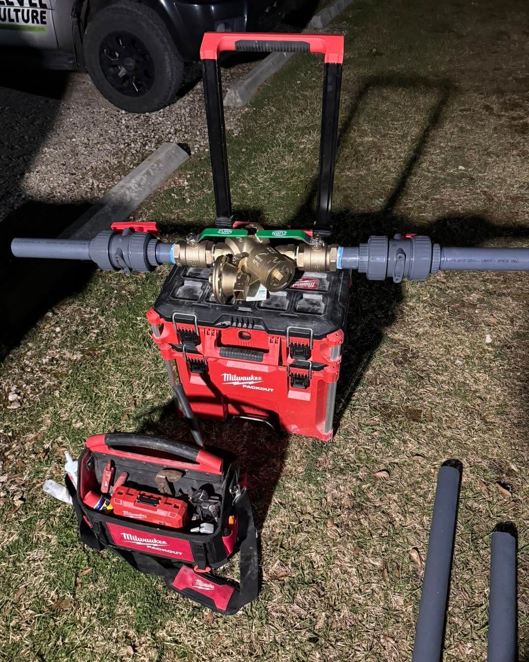 Red backpack leaf blower on grass at night, with a smaller red tool bag nearby.