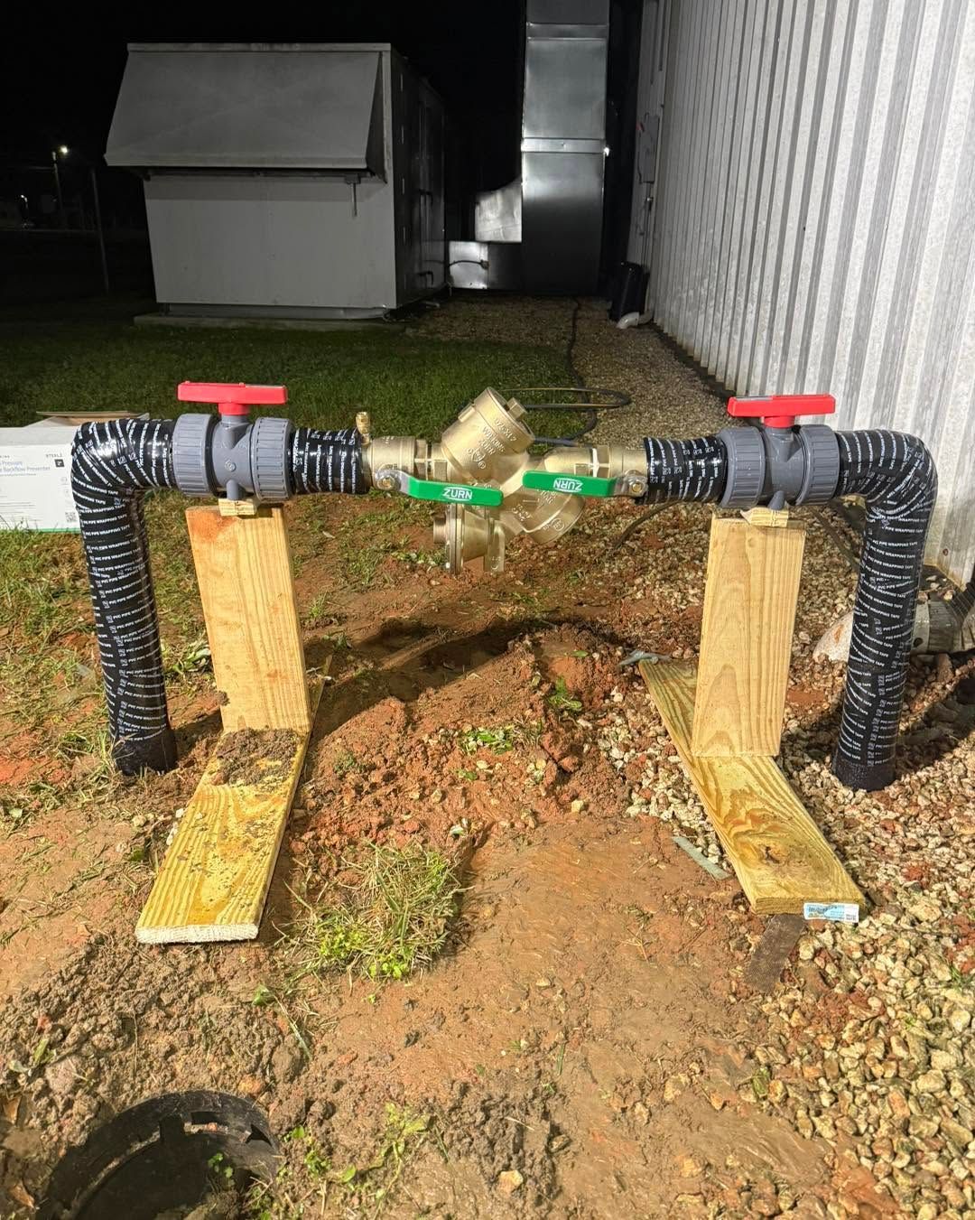 Backyard PVC pipe setup on wooden supports with red handles and green center valve at night