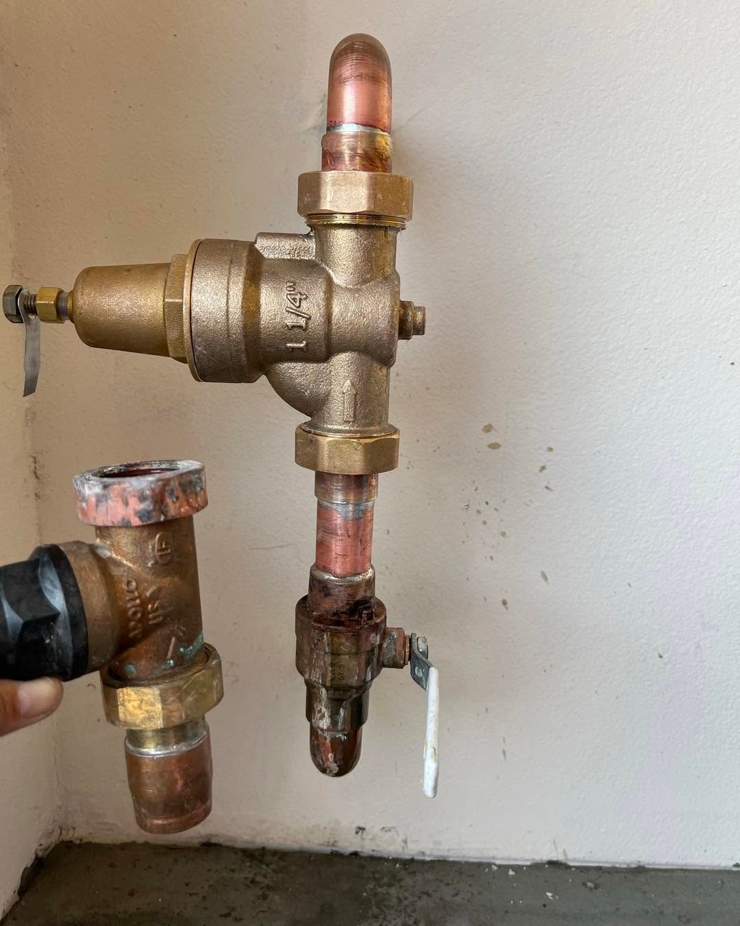Close-up of brass plumbing valves and pipes mounted on a wall, with a copper fitting at the top and a shutoff lever below