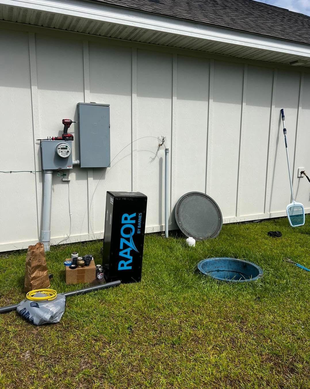 Backyard beside house with utility boxes, scattered tools, a blue net, and a round cover on the grass