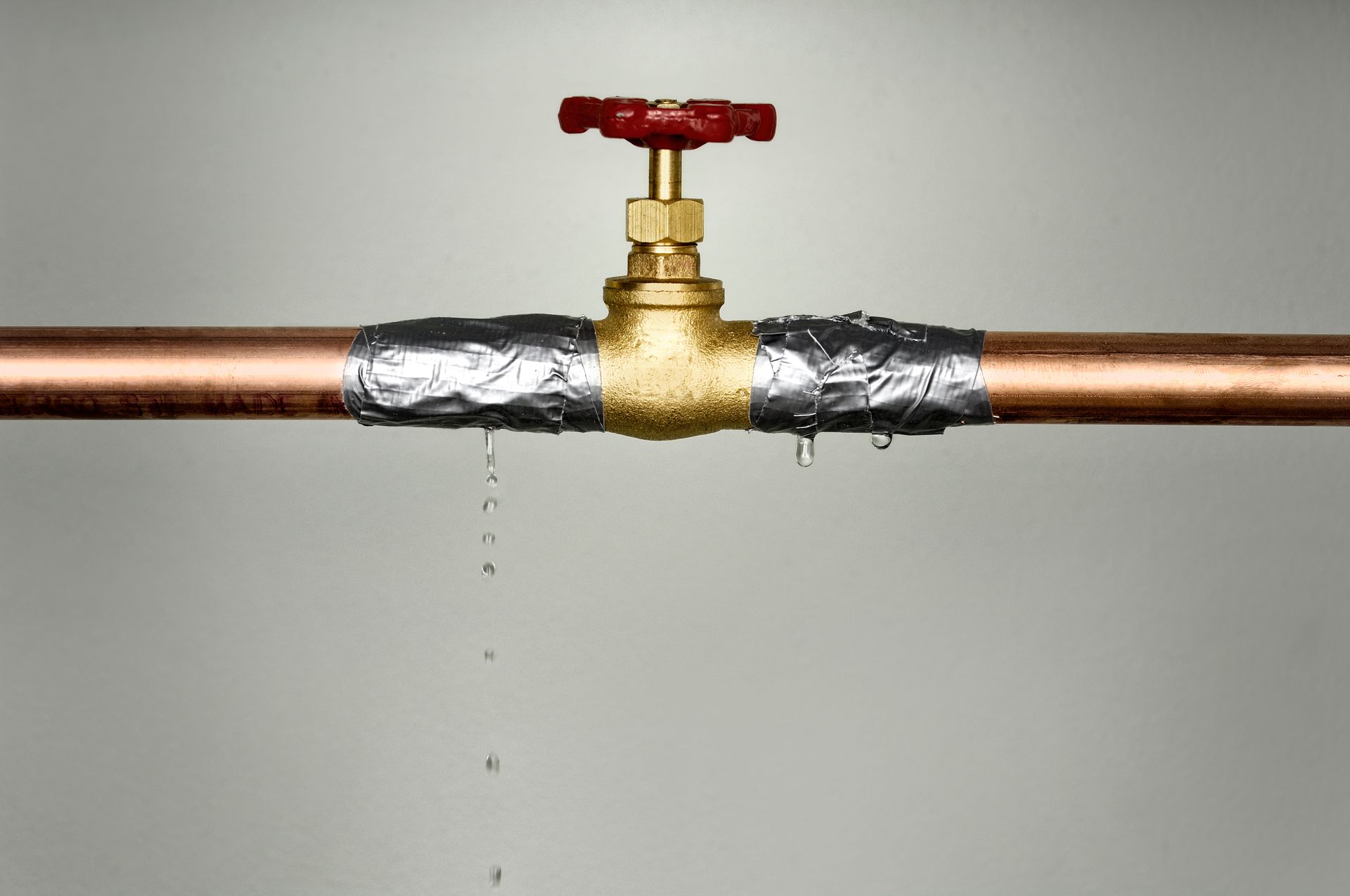Copper pipes with duct tape and a leaky valve; water drips.