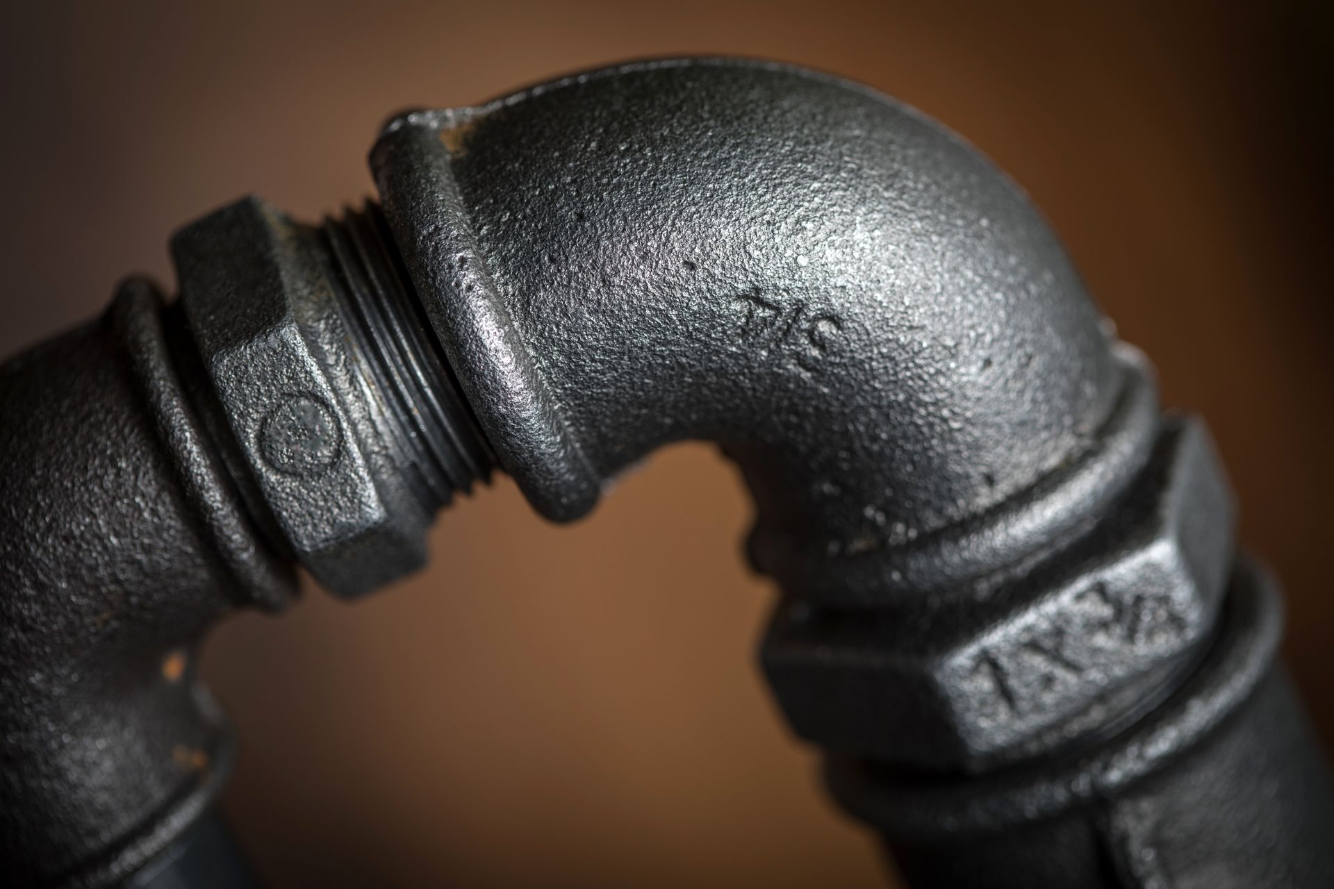 Close-up of black, textured pipe fittings joined at a 90-degree angle, against a brown background.