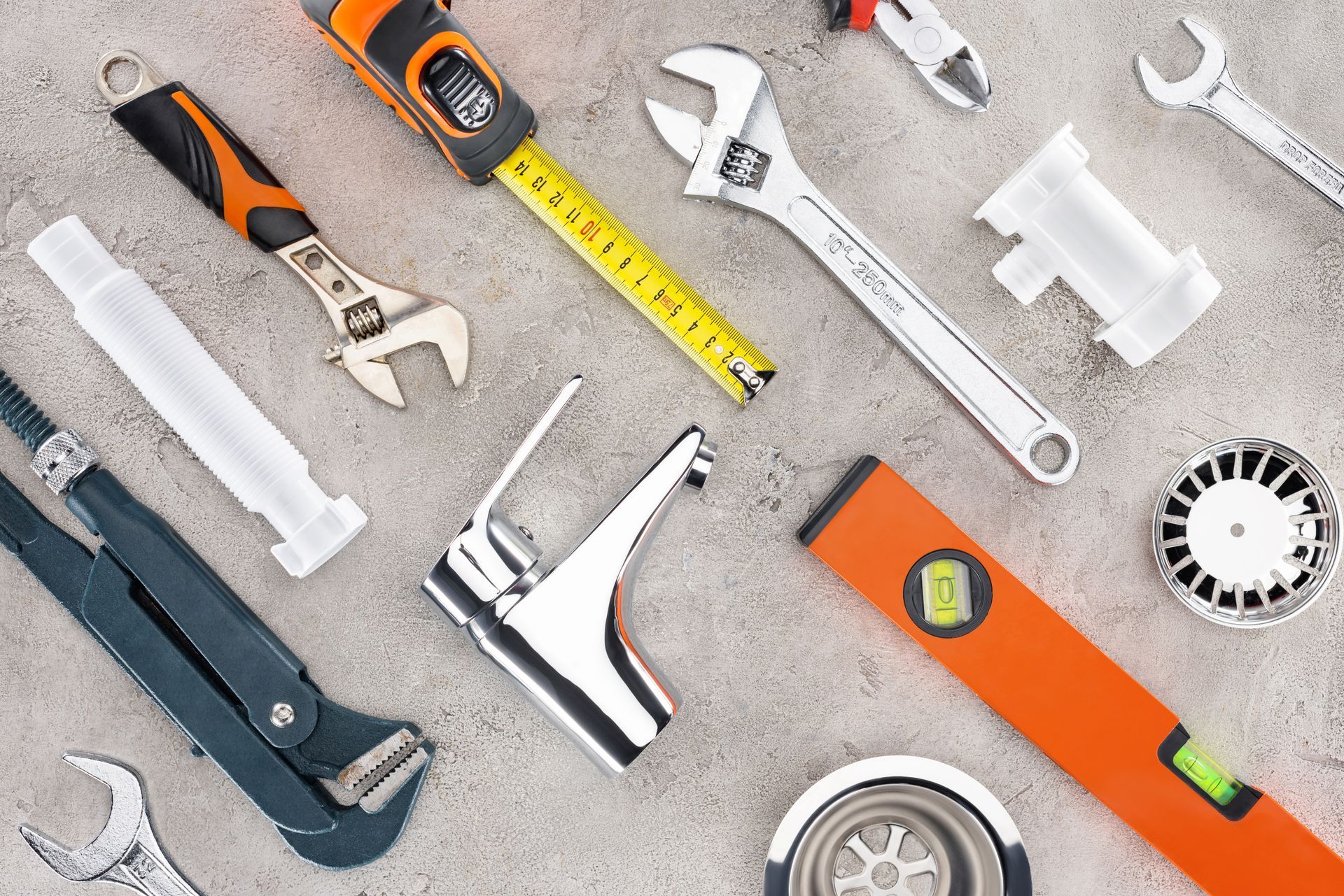 Tools for plumbing work, including wrenches, measuring tape, and a faucet, arranged on a gray surface.
