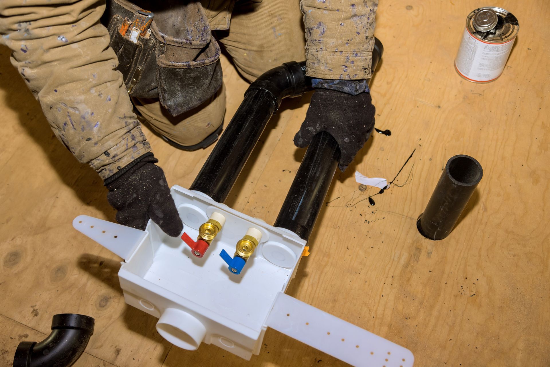 Person installing plumbing, connecting black pipes to a white box with red and blue faucet valves.