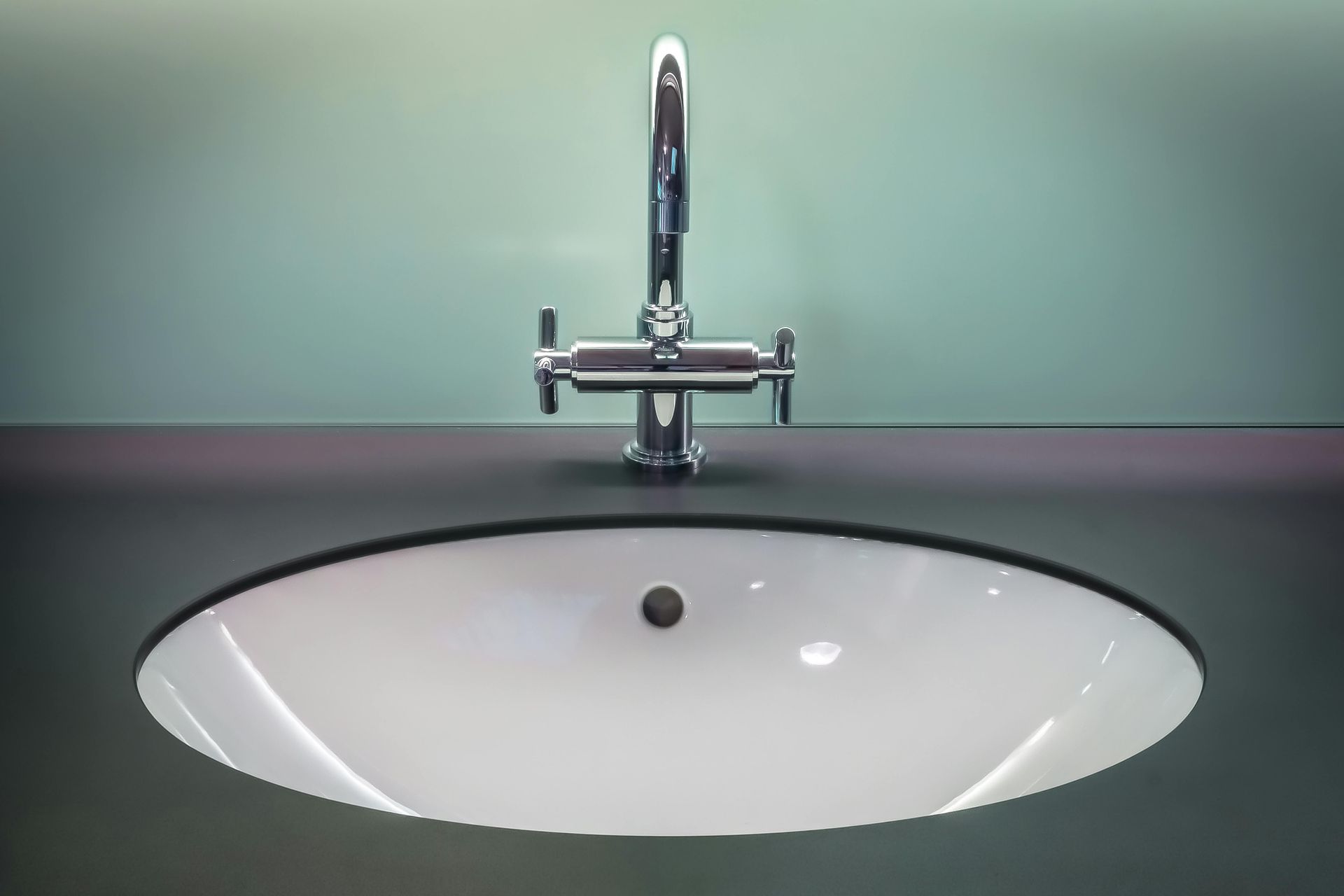 White oval sink with chrome faucet on a dark counter, light green wall.