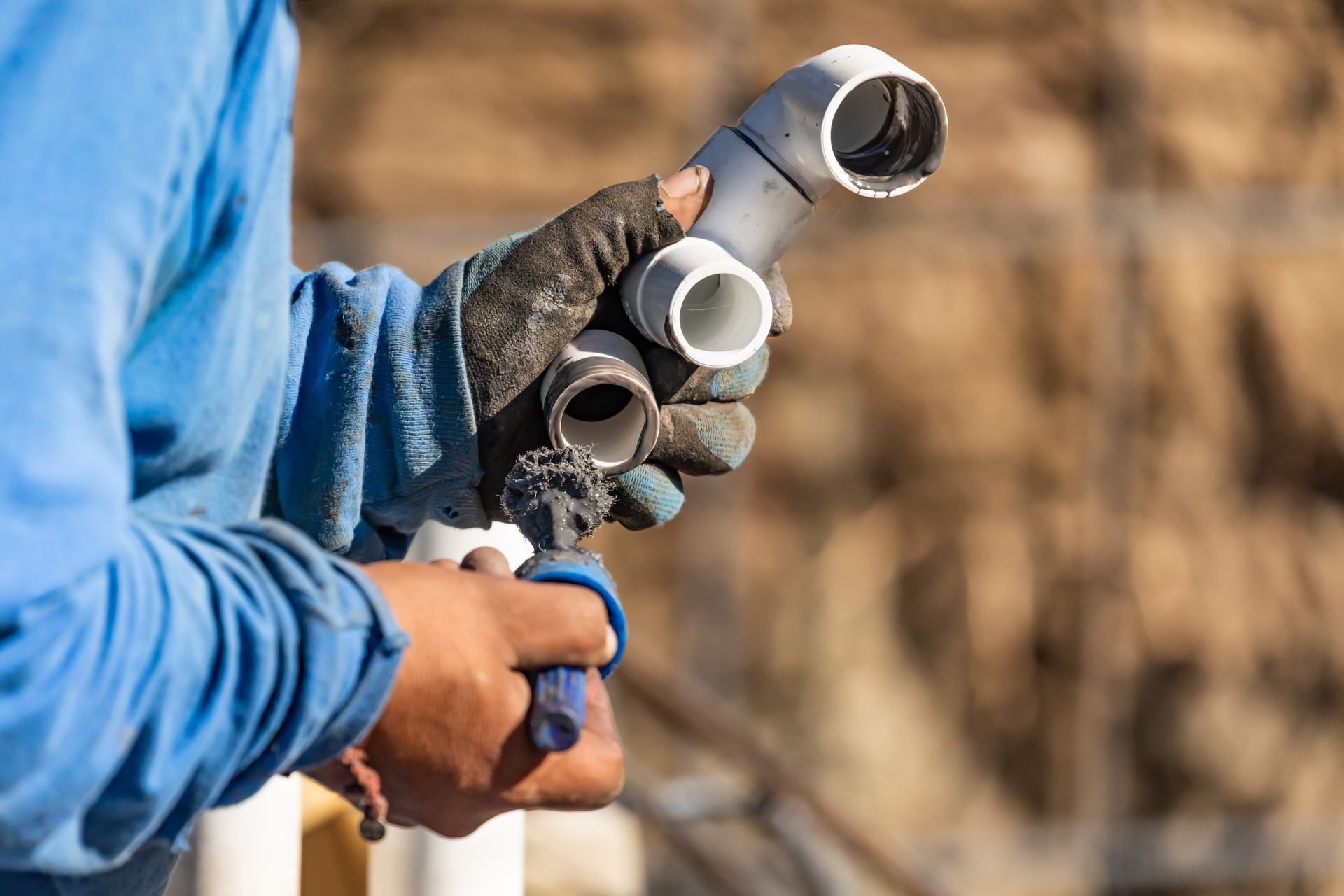 Person in blue shirt holding plumbing pipes outdoors.