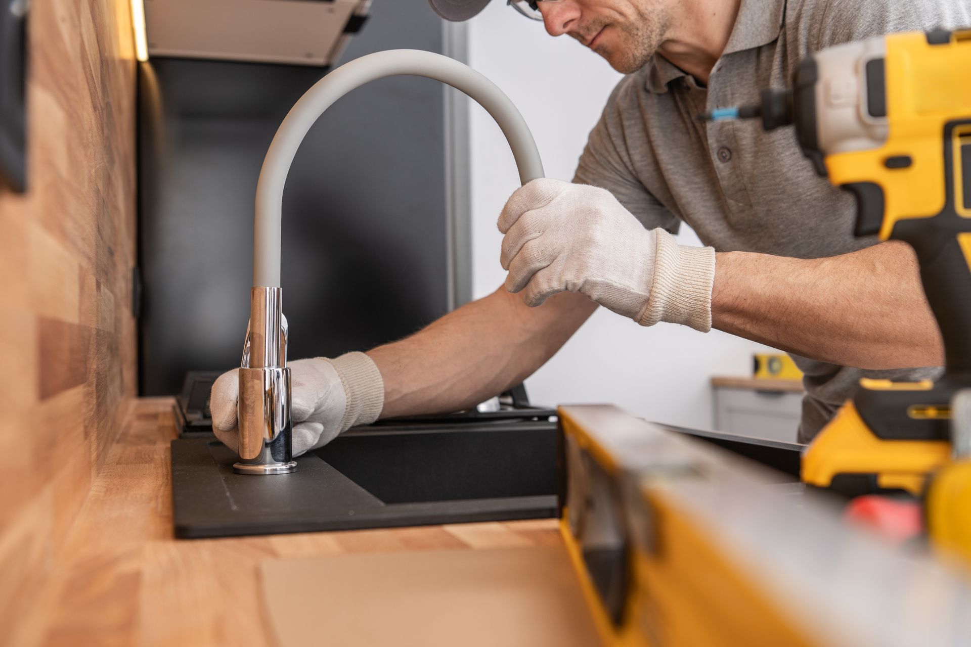 A person in gloves installs a kitchen faucet on a countertop.