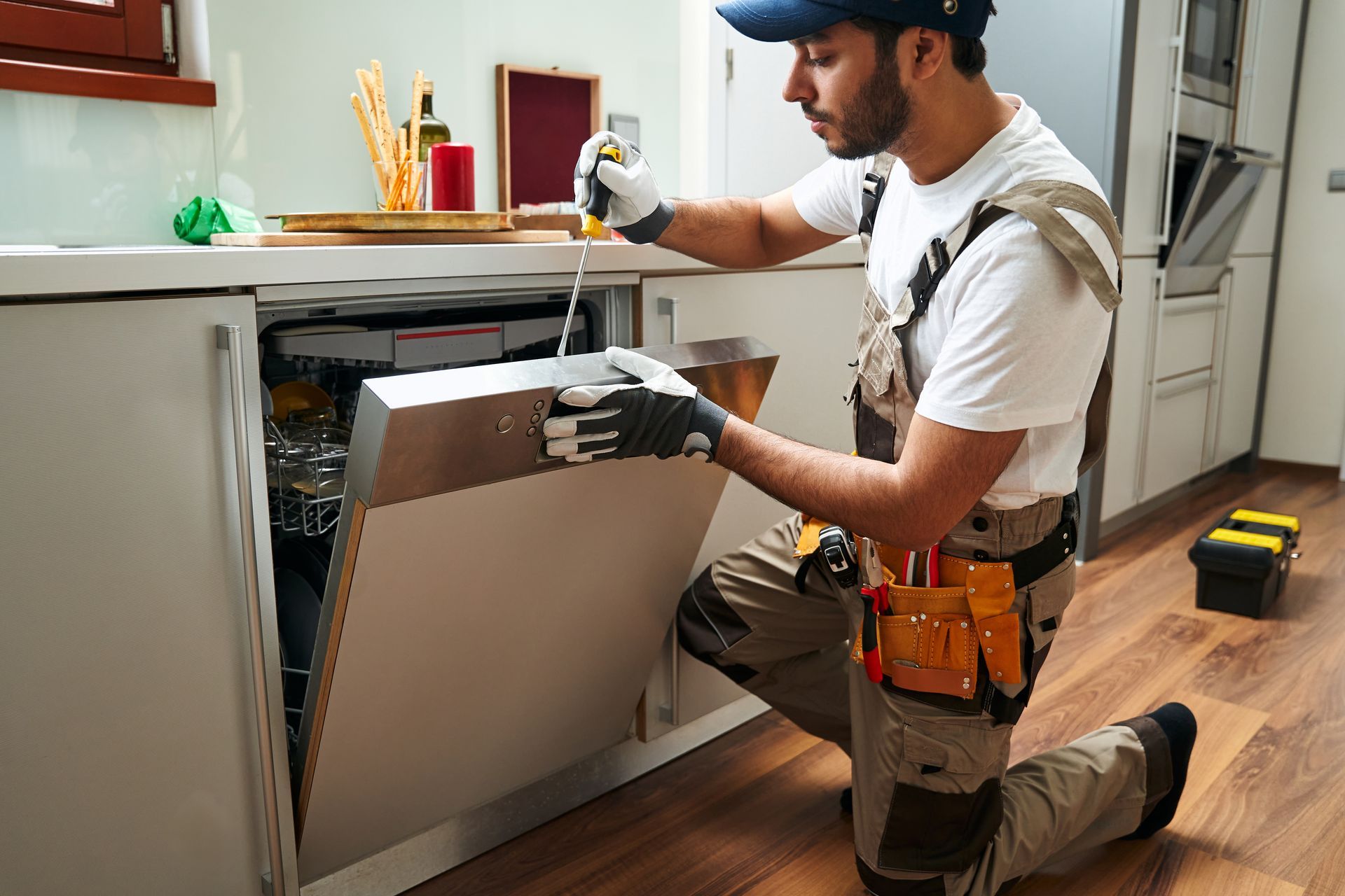 Man kneeling, fixing a dishwasher in a kitchen.