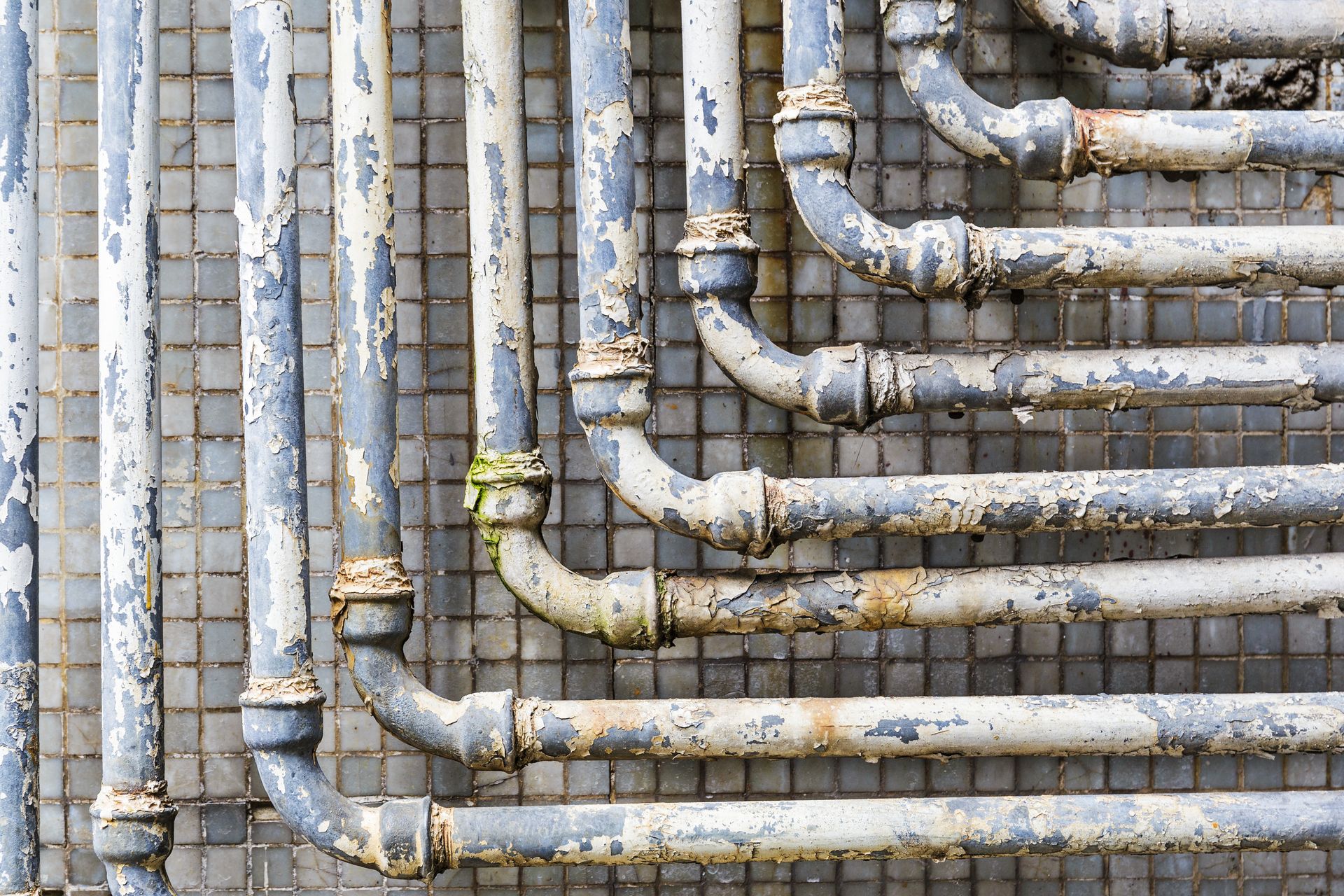 Old, peeling, gray pipes zig-zag against a tiled background.