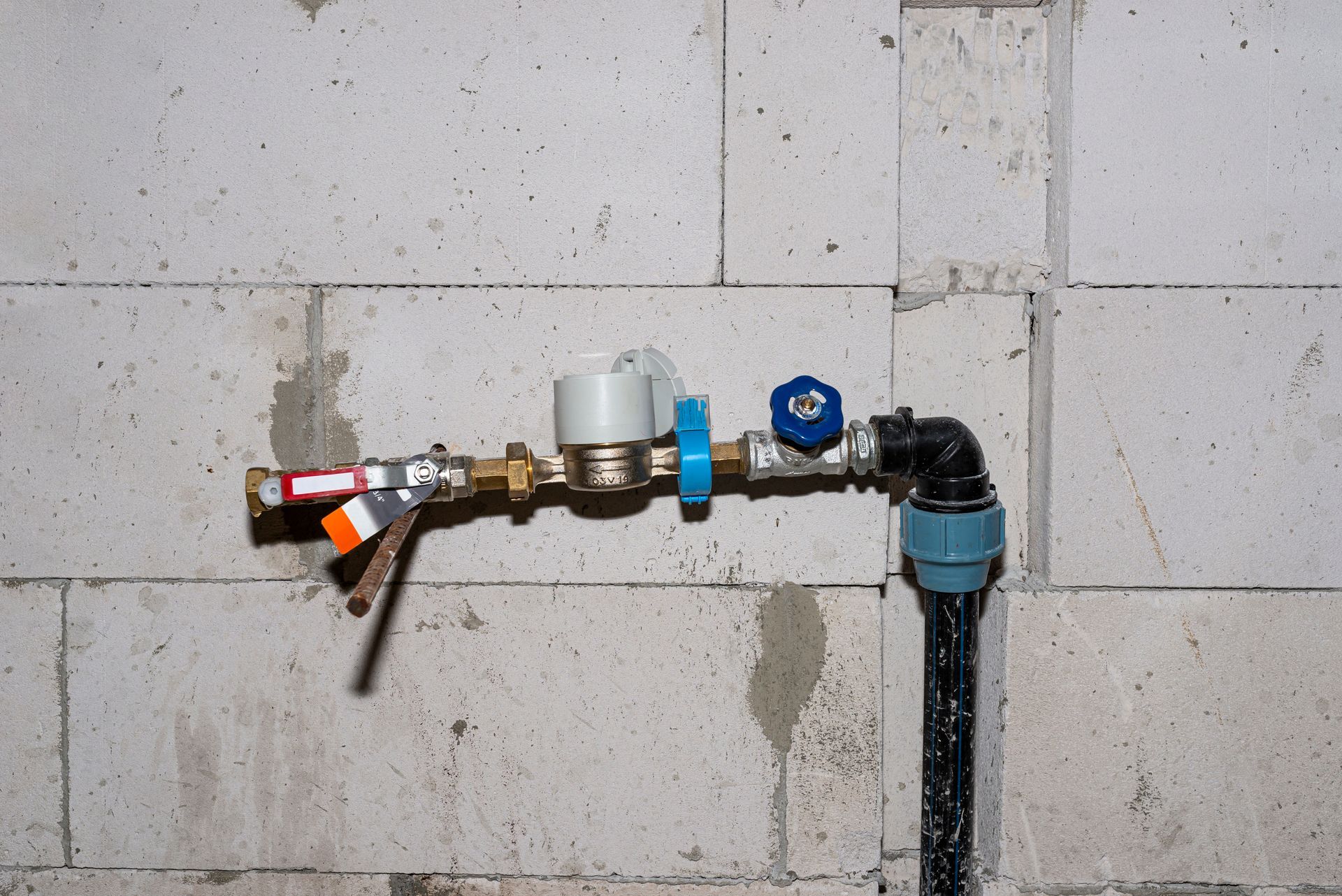 Piping system with valves and gauges attached to a white cinder block wall.