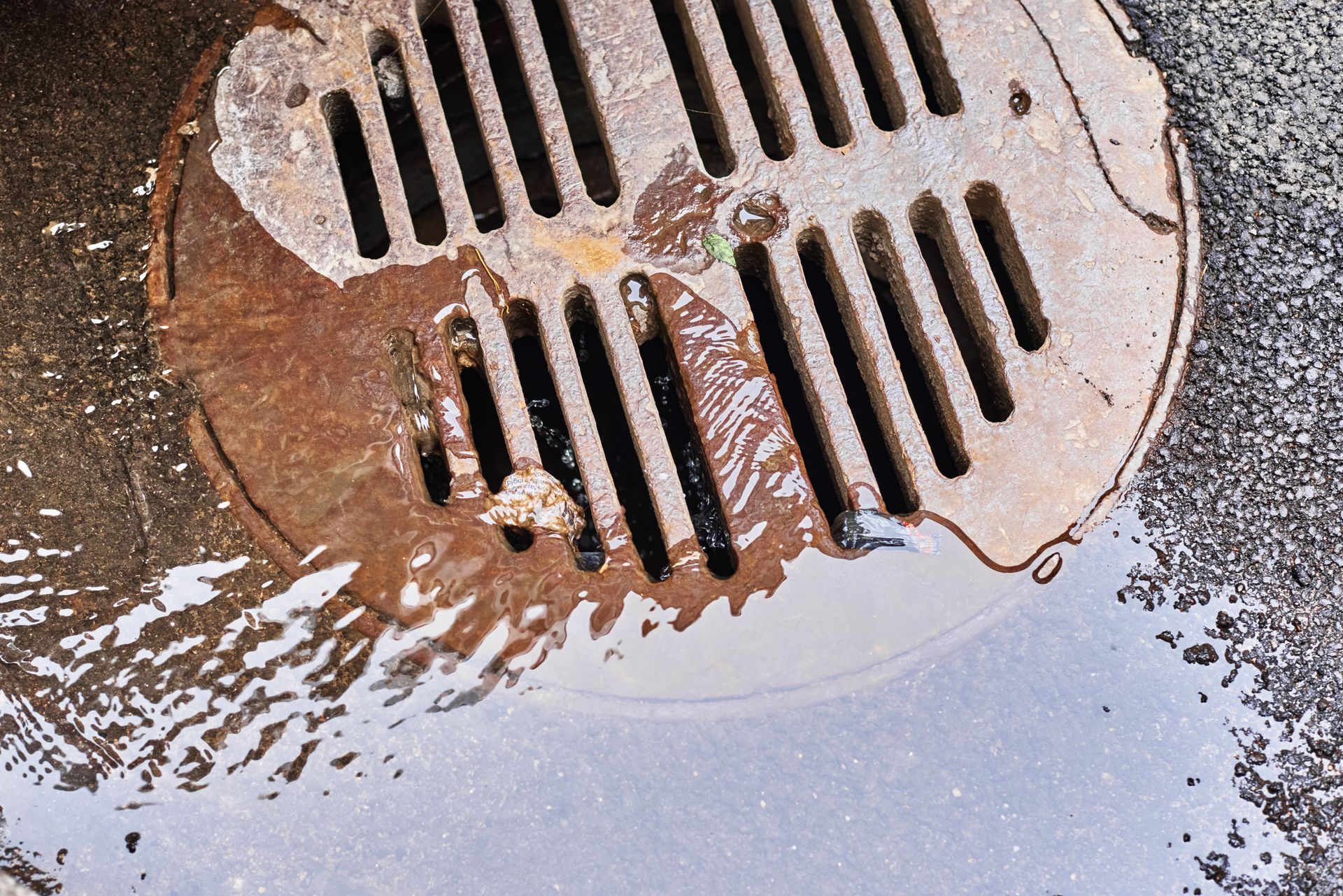 Overflowing rusty metal drain with water.