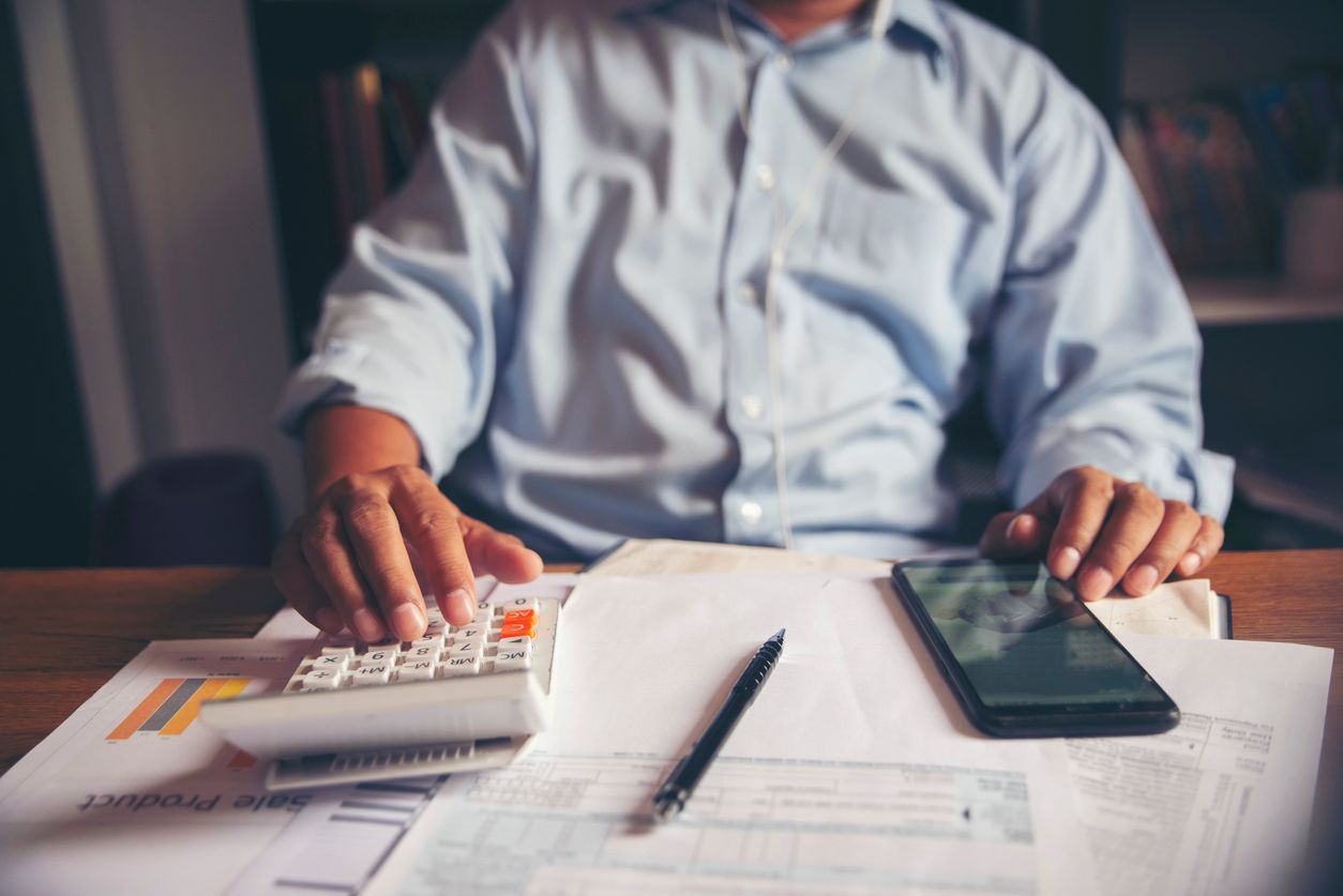 A man is sitting at a table using a calculator and a cell phone.
