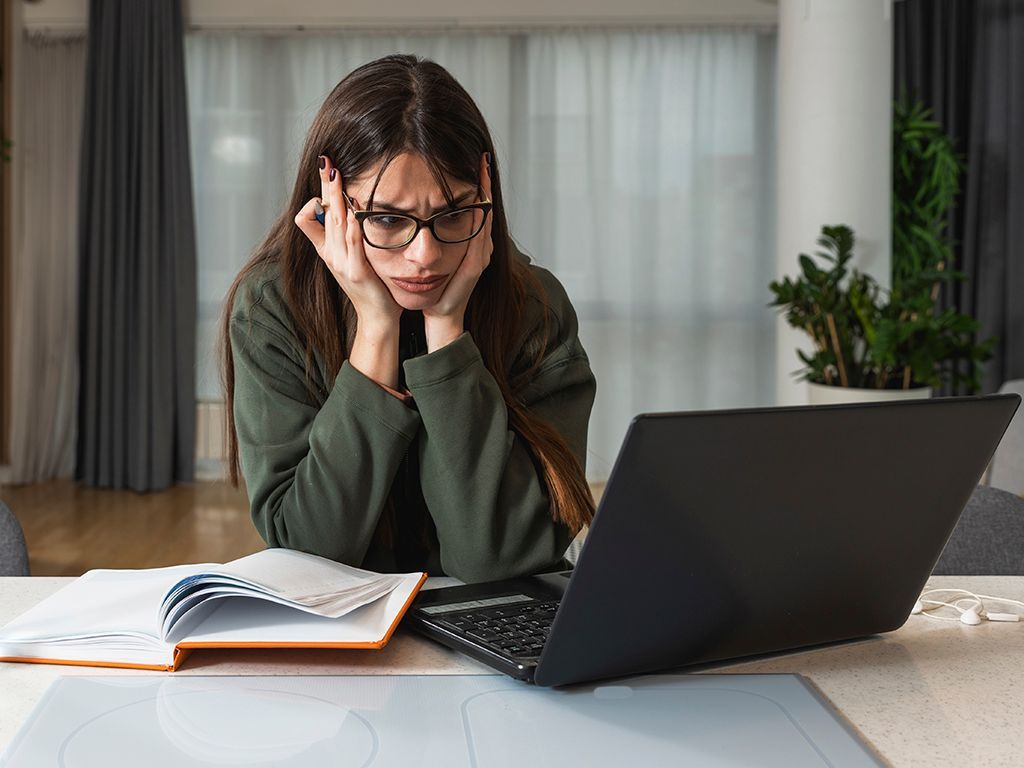 A woman is sitting at a table looking at a laptop computer.